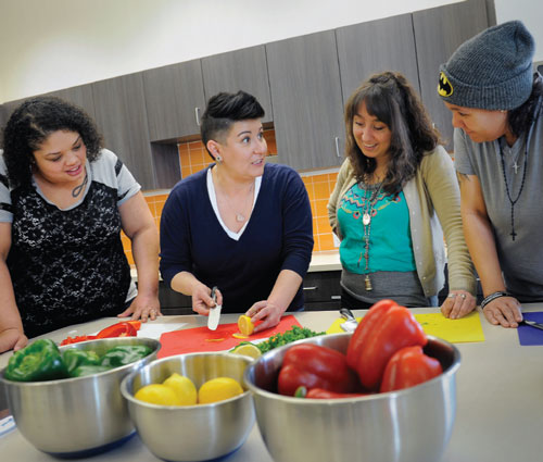 Image of four women cooking together with fresh fruits and vegetables in the Dahlia Campus for Health & Well-Being kitchen.