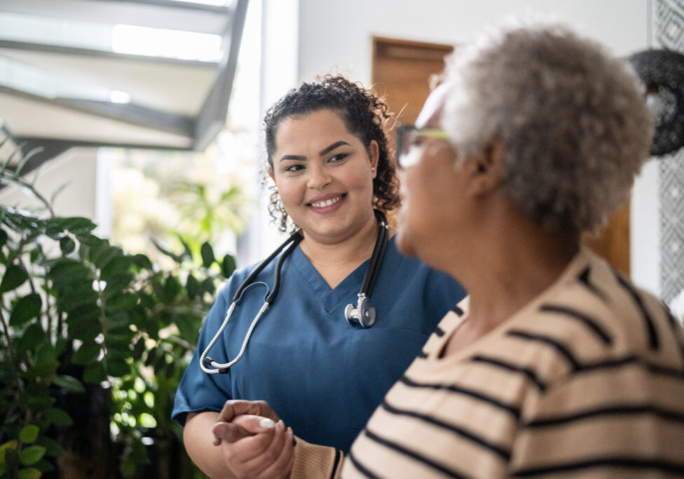 Home caregiver helping senior woman walking at home