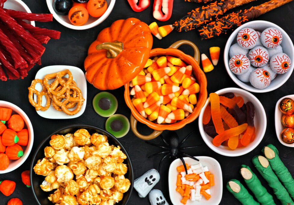 Halloween candy buffet table scene over a black stone background. Assortment of sweet, spooky treats. Above view.