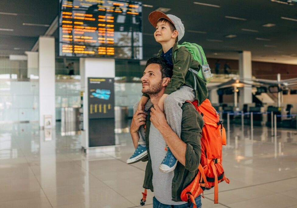 Photo of a cheerful little boy and his father, who travel together waiting for their flight at the airport